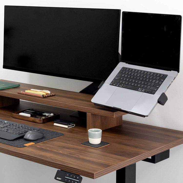 Silver Desky Expandable Laptop Mount holding a laptop next to a monitor on a dark wood desk.