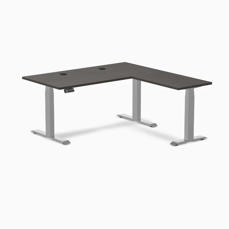 Desky L-Shape Laminate Sit Stand Desk in Burnished Wood with Gray frame and grommets.