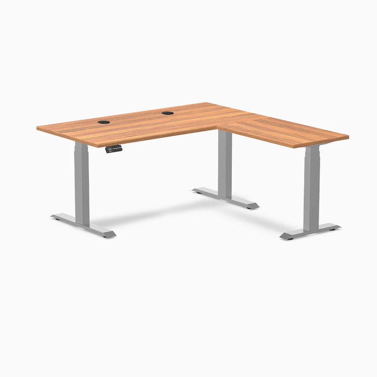 Desky L-Shape Laminate Sit Stand Desk in Prime Oak with gray frame and grommets.