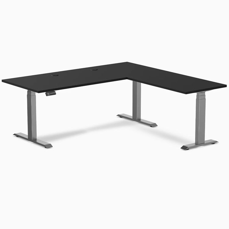 Black laminate L-shape sit-stand desk with space gray adjustable legs and grommets.