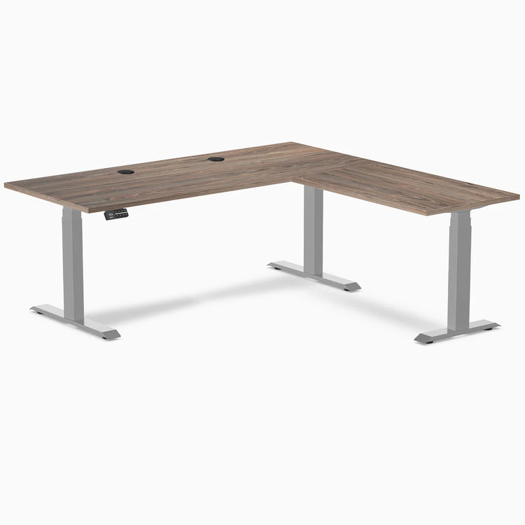 Natural Walnut L-Shape Laminate Sit Stand Desk with gray frame and grommets.