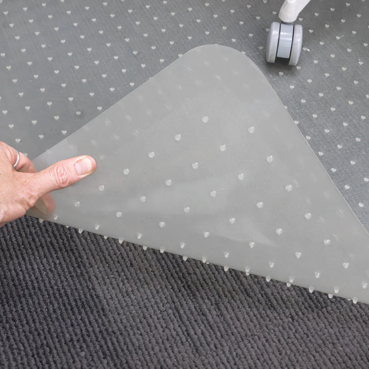 Hand lifting a corner of a translucent Desky Chair Mat with studded underside on gray carpet.
