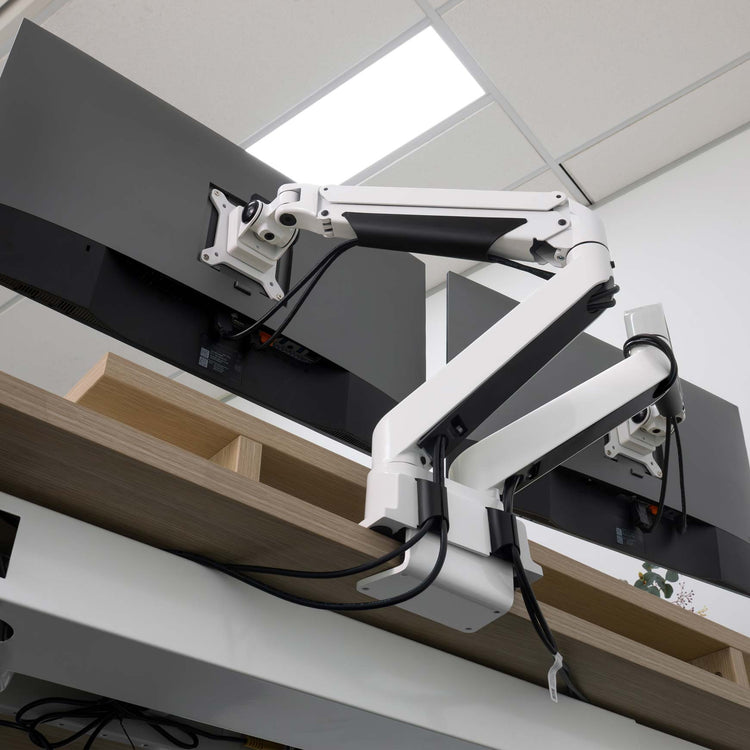 White Desky Dual Monitor Arm with black accents, clamping to a light wood desk, supporting two dark monitors.