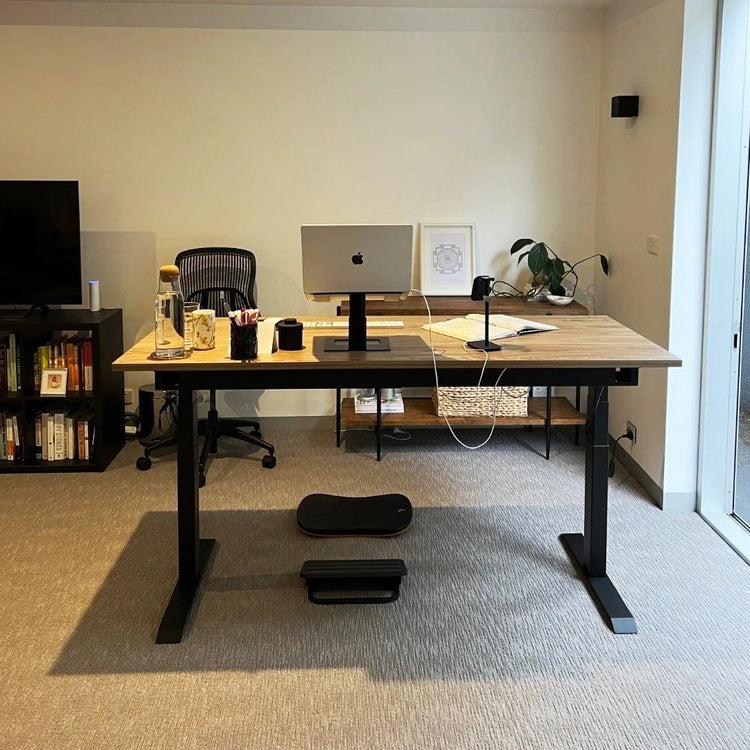Matte black Desky Balance Board with dimpled footpads under a standing desk in a modern office.