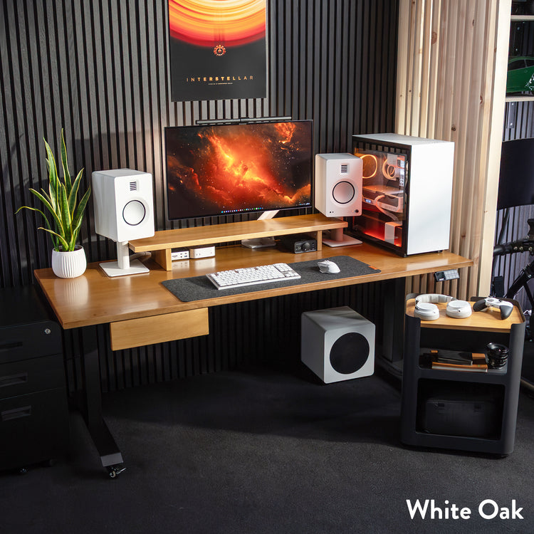 White Oak Desky Dual Hardwood Sit Stand Desk with black legs, monitor, speakers, and gaming PC setup.