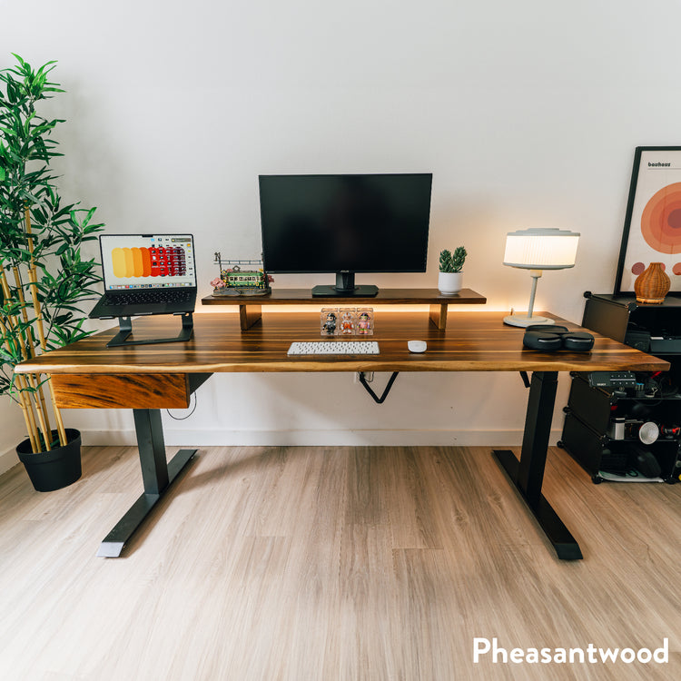Pheasantwood hardwood standing desk with black legs, integrated drawer, monitor riser, and organized workspace.