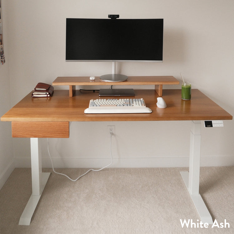 White ash hardwood standing desk with a matching drawer, white legs, and monitor riser.