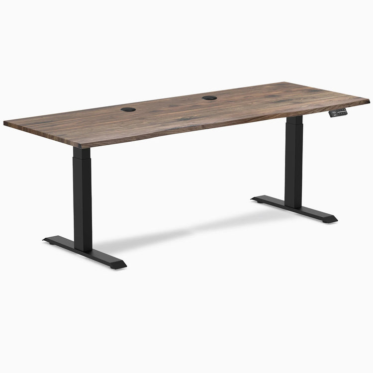Desky Dual sit-stand desk with natural walnut laminate top, matte black frame, and two grommets.
