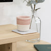 Light grey felt coaster with a pink and white ceramic mug on a light wood desk.