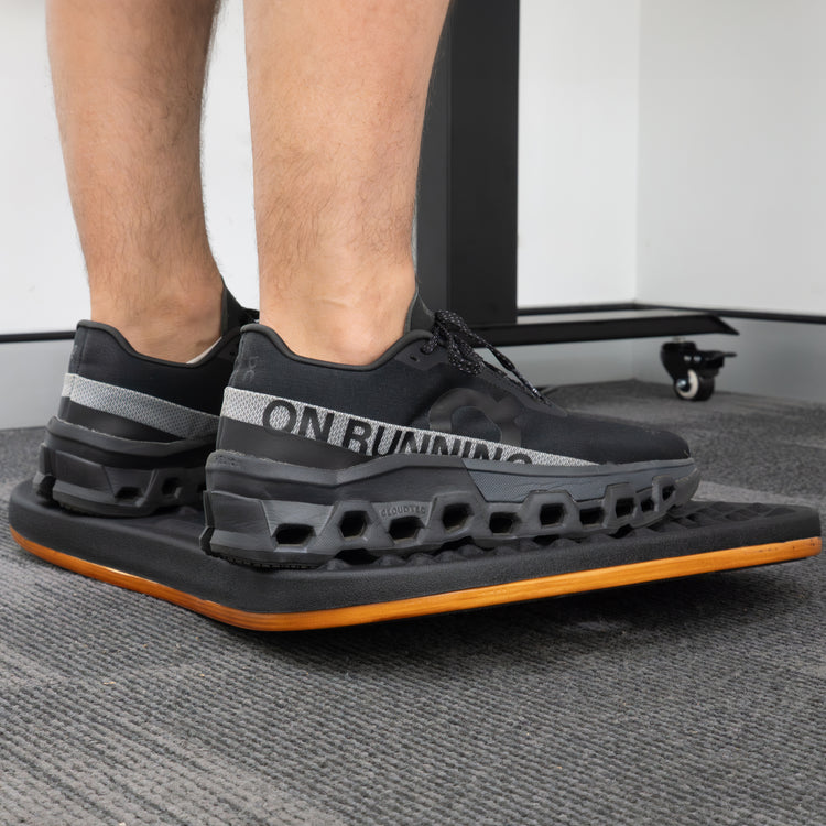 Person standing on a black and orange Desky Balance Board with dimpled footpads.