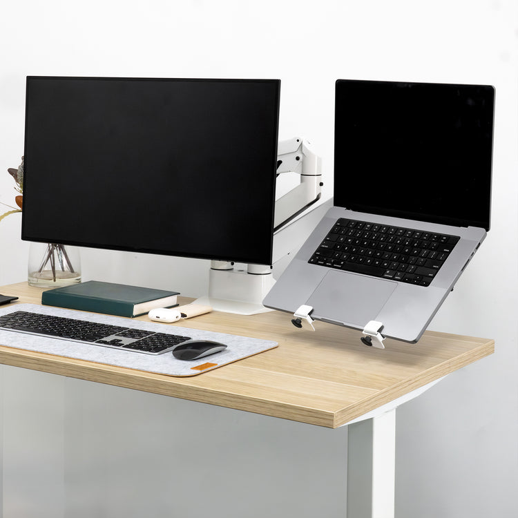 Silver laptop on a white Desky Universal Laptop Mount next to a monitor, both on a desk.