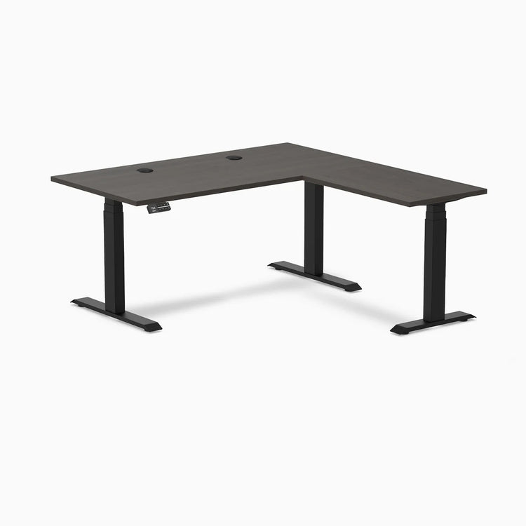 Desky L-Shape Laminate Sit Stand Desk in burnished wood with matte black legs and grommets.
