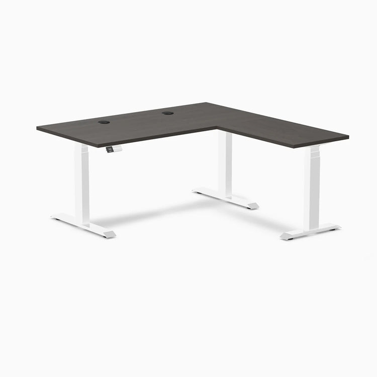 Desky L-Shape Laminate Sit Stand Desk in Burnished Wood with white legs and grommets.