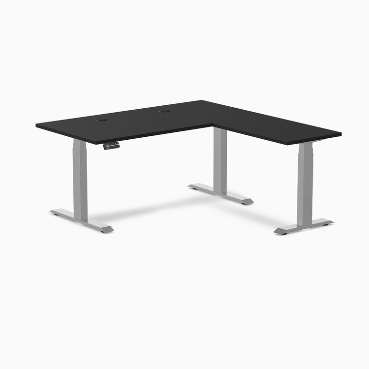 Black laminate L-shaped sit-stand desk with gray adjustable legs and grommets.