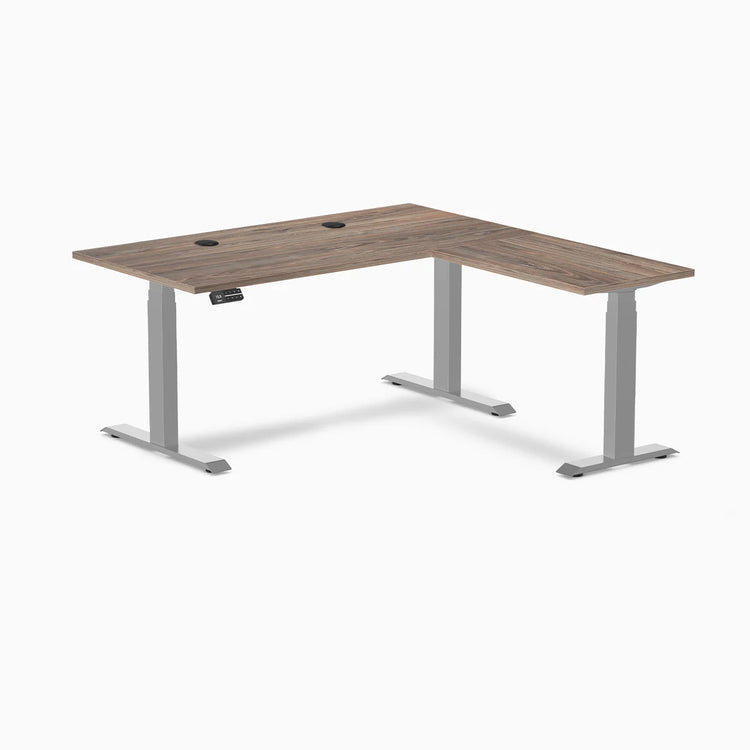 Natural Walnut Desky L-Shape Laminate Sit Stand Desk with gray frame and grommets.