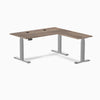 Natural Walnut Desky L-Shape Laminate Sit Stand Desk with gray frame and grommets.