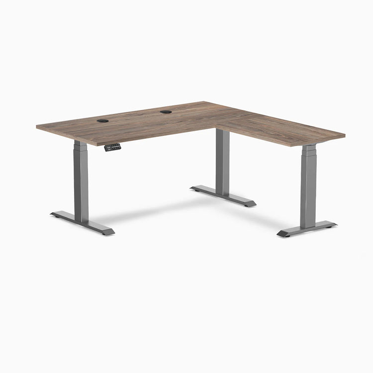 Desky L-Shape Laminate Sit Stand Desk in Natural Walnut with Space Gray frame and grommets.