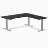 Black laminate L-shape sit-stand desk with gray adjustable legs and grommets.
