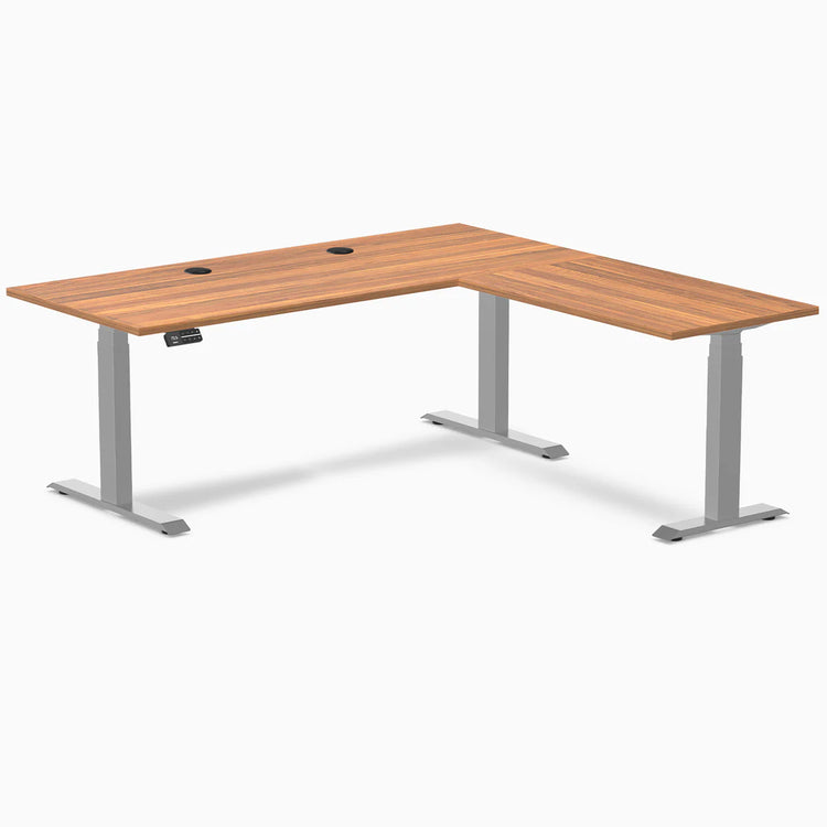 Prime Oak laminate L-shape sit-stand desk with gray frame and grommets.