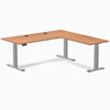Prime Oak laminate L-shape sit-stand desk with gray frame and grommets.