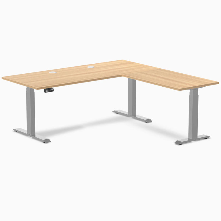 Sublime Teak L-Shape laminate sit-stand desk with gray frame, grommets, and control panel.