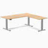 Sublime Teak L-Shape laminate sit-stand desk with gray frame, grommets, and control panel.