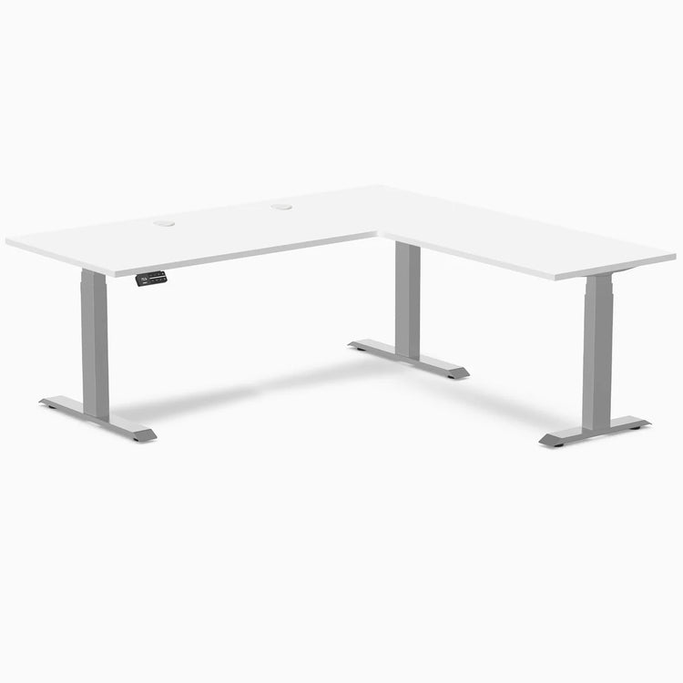 White laminate L-shaped sit-stand desk with gray adjustable legs and grommets.