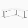 White laminate L-shaped sit-stand desk with gray adjustable legs and grommets.