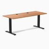 Desky Zero fixed-height office desk with Prime Oak laminate top, two grommets, and matte black steel frame.