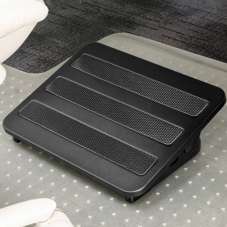 Black Desky Classic Foot Rest with three textured non-skid panels, on a clear mat over dark carpet.