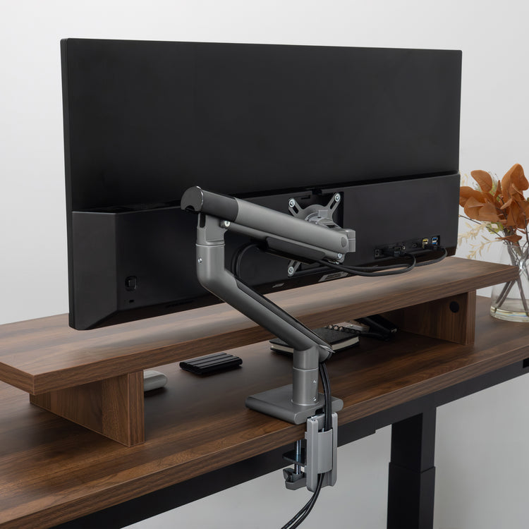 Desky Single Slim Aluminium Monitor Arm in space gray, mounted to a wooden desk.