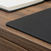 Desky black leather desk mat with pebbled texture on a wooden desk, notebook in background.