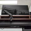 Black Desky Single Monitor Arm securely mounted to a dark wood desk, supporting a large black monitor.