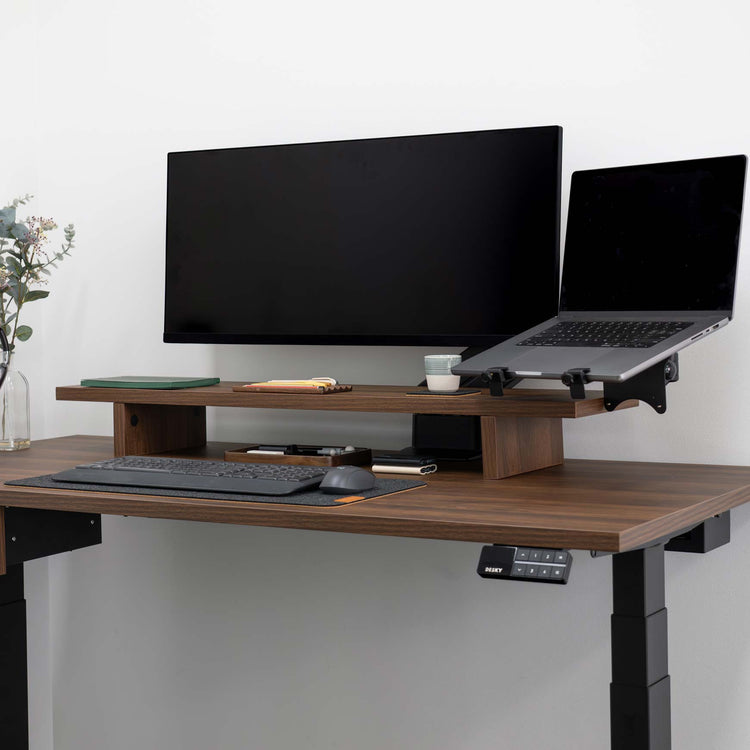 Dark wood standing desk with a black laptop mounted on a VESA arm next to a monitor.