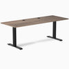 Desky Zero fixed height office desk with natural walnut laminate top, grommets, and matte black steel frame.