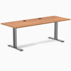 Desky Zero fixed-height office desk with Prime Oak laminate top, Space Gray steel frame, and two grommets.