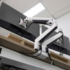 White Desky Dual Monitor Arm with black accents, clamping to a light wood desk, supporting two dark monitors.
