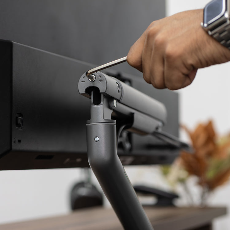 Hand adjusting a dark gray Desky Single Slim Aluminium Monitor Arm with a hex key.