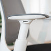 Close-up of Desky Pulse supportive desk chair's white 4D adjustable armrest with gray pad and mesh back.