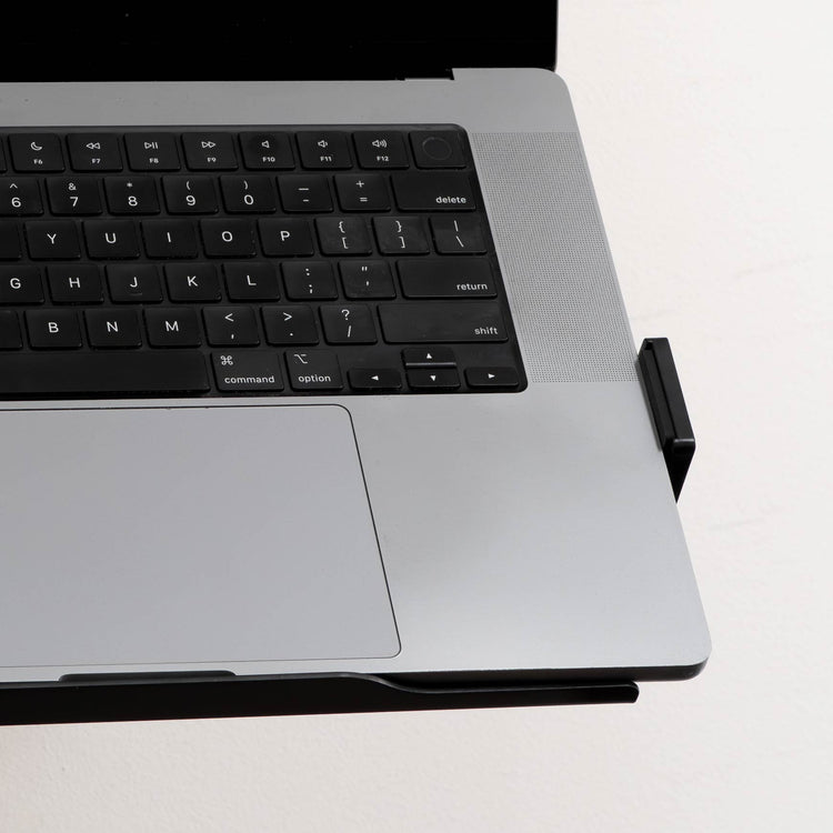 Silver laptop securely held by a black Desky Expandable Laptop Mount with silicone pads.