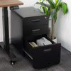 Black steel Desky 3-drawer mobile filing cabinet with rounded edges, one drawer open, next to a standing desk.