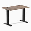 Desky Zero Mini sit-stand desk with natural walnut top, black fixed-height legs, and grommets.