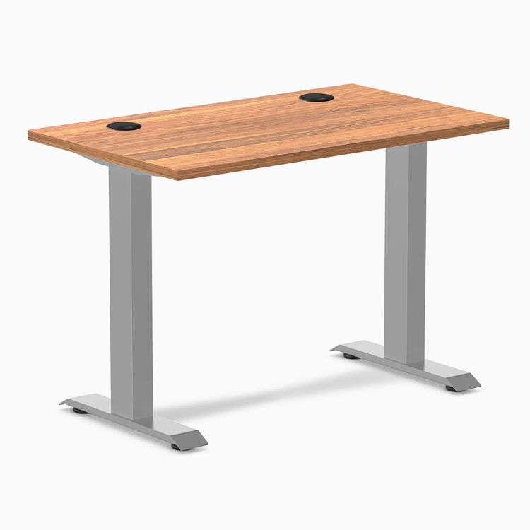 Desky Zero Mini fixed-height desk with Prime Oak top, gray legs, and two black grommets.