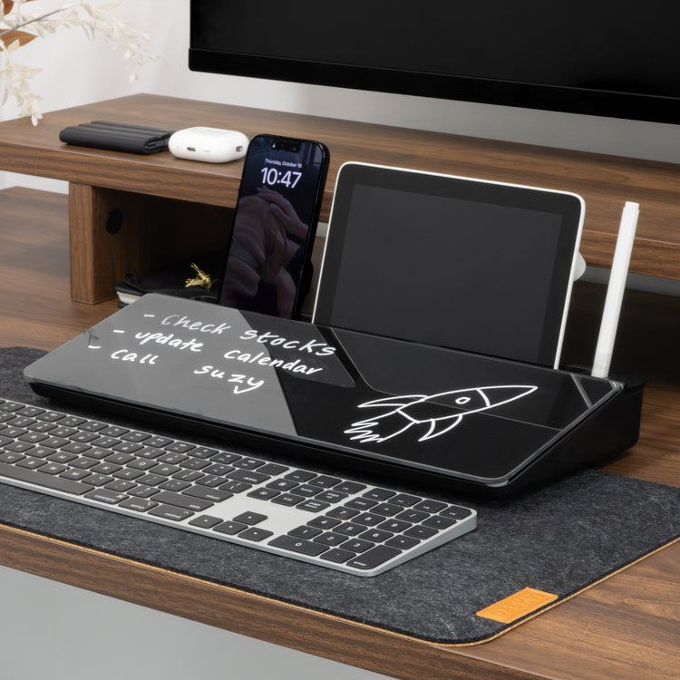 Black glass Desky Desktop Whiteboard with storage, holding a phone, tablet, and stylus on a wooden desk.