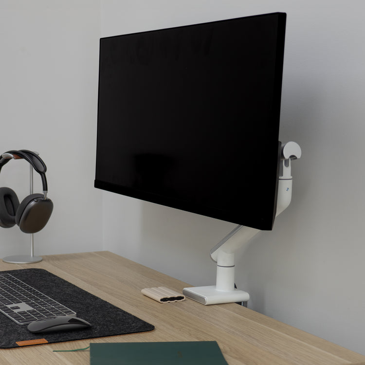 White Desky Single Slim Aluminium Monitor Arm holding a black monitor on a light wood desk.