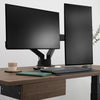 Black Desky Dual Monitor Arm supporting two screens on a dark wood desk with a keyboard and notebook.