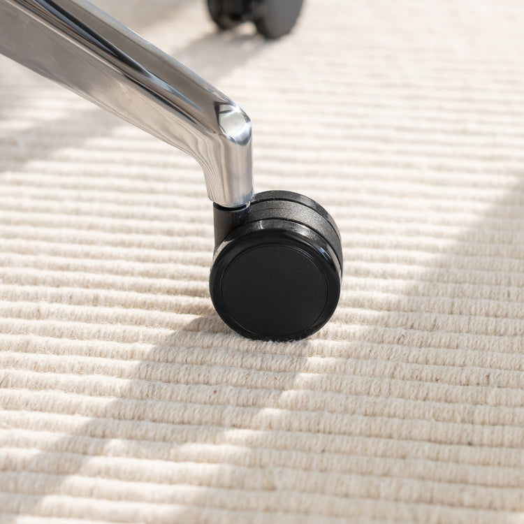 Chrome die-cast aluminum base and black caster wheel of a Desky Pinnacle office chair on a textured rug.