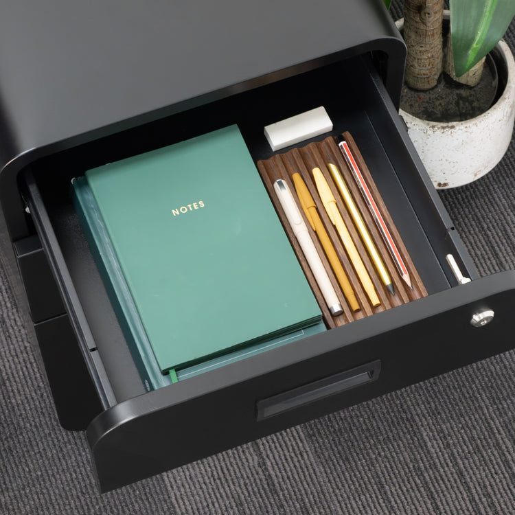 Black Desky 3-drawer mobile filing cabinet with a soft-close top drawer open, showing a green notebook and pens.