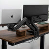 Black Desky universal laptop mount and monitor arm holding a silver laptop and black monitor on a dark wood desk.
