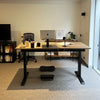 Matte black Desky Balance Board with dimpled footpads under a standing desk in a modern office.